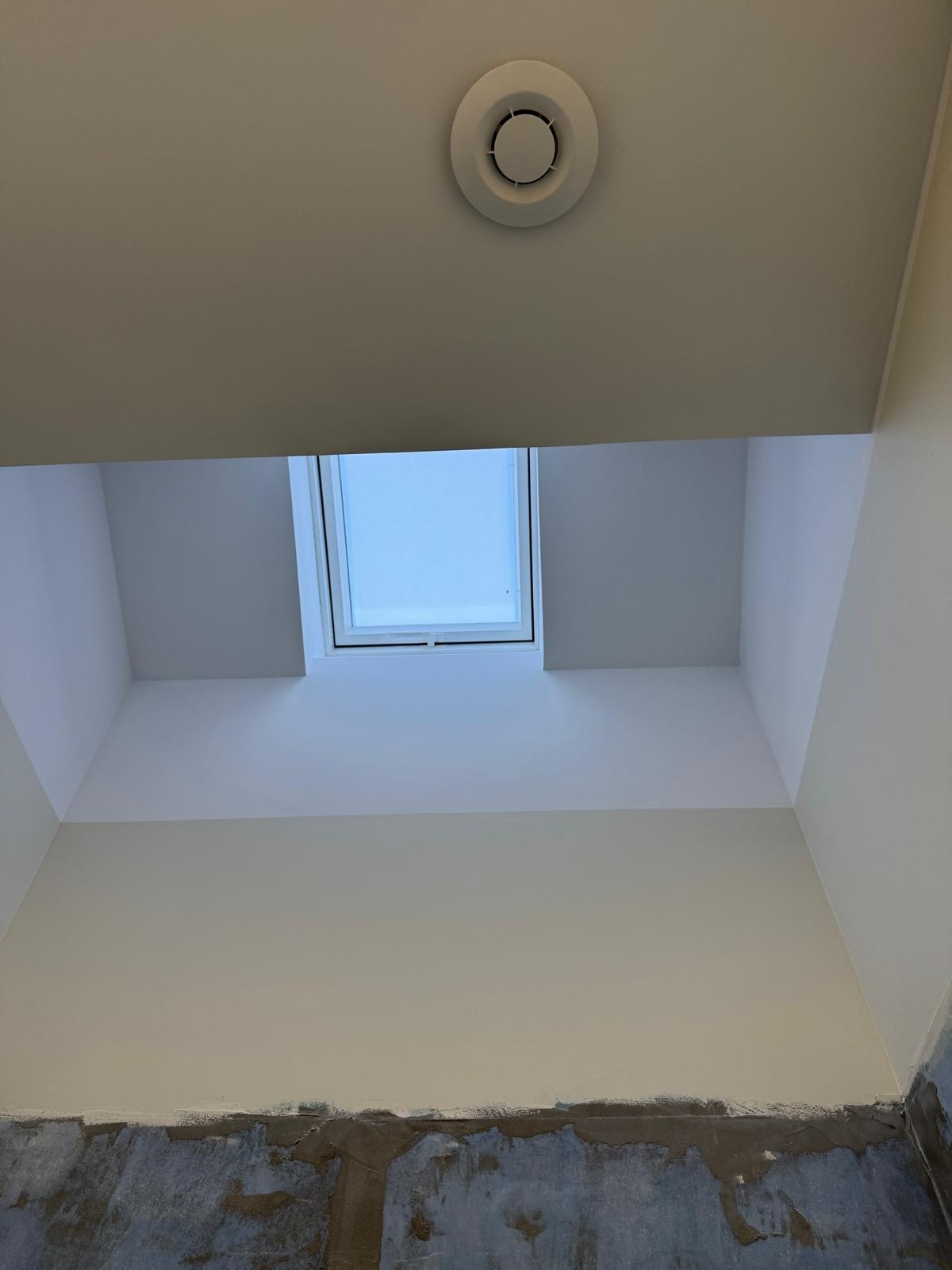 Wnętrze w trakcie remontu: widok na sufit z oknem dachowym i kratką wentylacyjną, ściany częściowo pomalowane, dolna część ściany w stanie surowym.