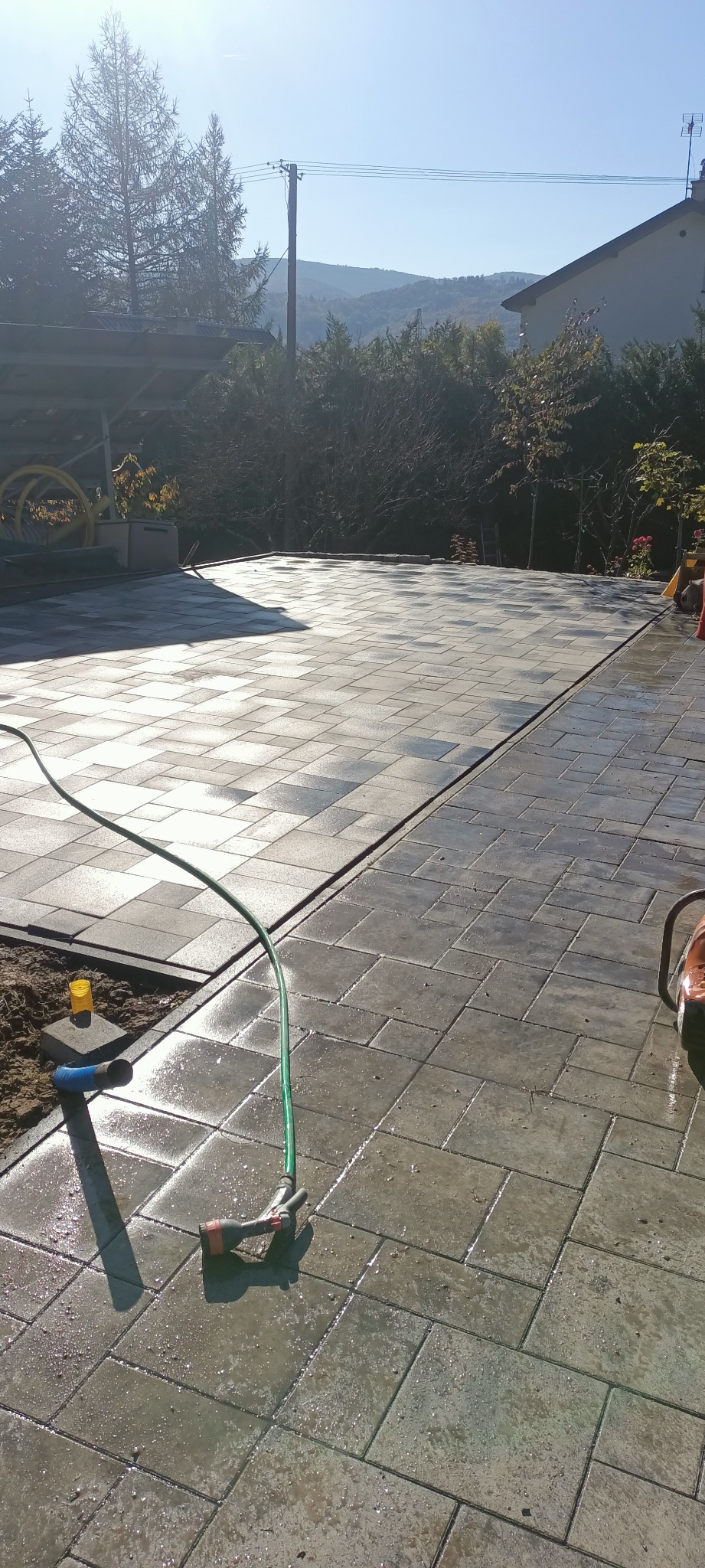 Ułożona kostka brukowa na posesji w Szczyrku, widok z góry. Świeżo umyta powierzchnia, widoczny wąż ogrodowy i elementy otoczenia.