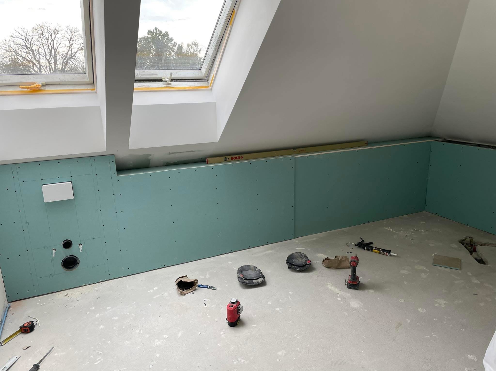 Poddasze z oknami dachowymi w trakcie zabudowy płytami gipsowo-kartonowymi. Widoczne narzędzia i poziomica. Ściany w kolorze zielonym.