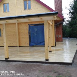PPHU ROBMAX MEBLE - Wykończony taras z jasnych płytek przy drewnianym domu z elementami z cegły. Widoczna konstrukcja zadaszenia tarasu z drewnianych belek.