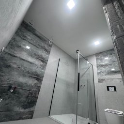 Elektryk Kacper Działo - Nowoczesna kabina prysznicowa z grafitową ścianą w wykończonej łazience, widok z dołu, kwadratowe oświetlenie sufitowe, wisząca toaleta.