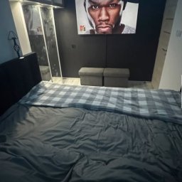 Elektryk Kacper Działo - Nowoczesna sypialnia z podświetleniem LED sufitu, reflektorami i czarną ścianą z wizerunkiem 50 Centa. Minimalistyczny design, łóżko z szarą pościelą.