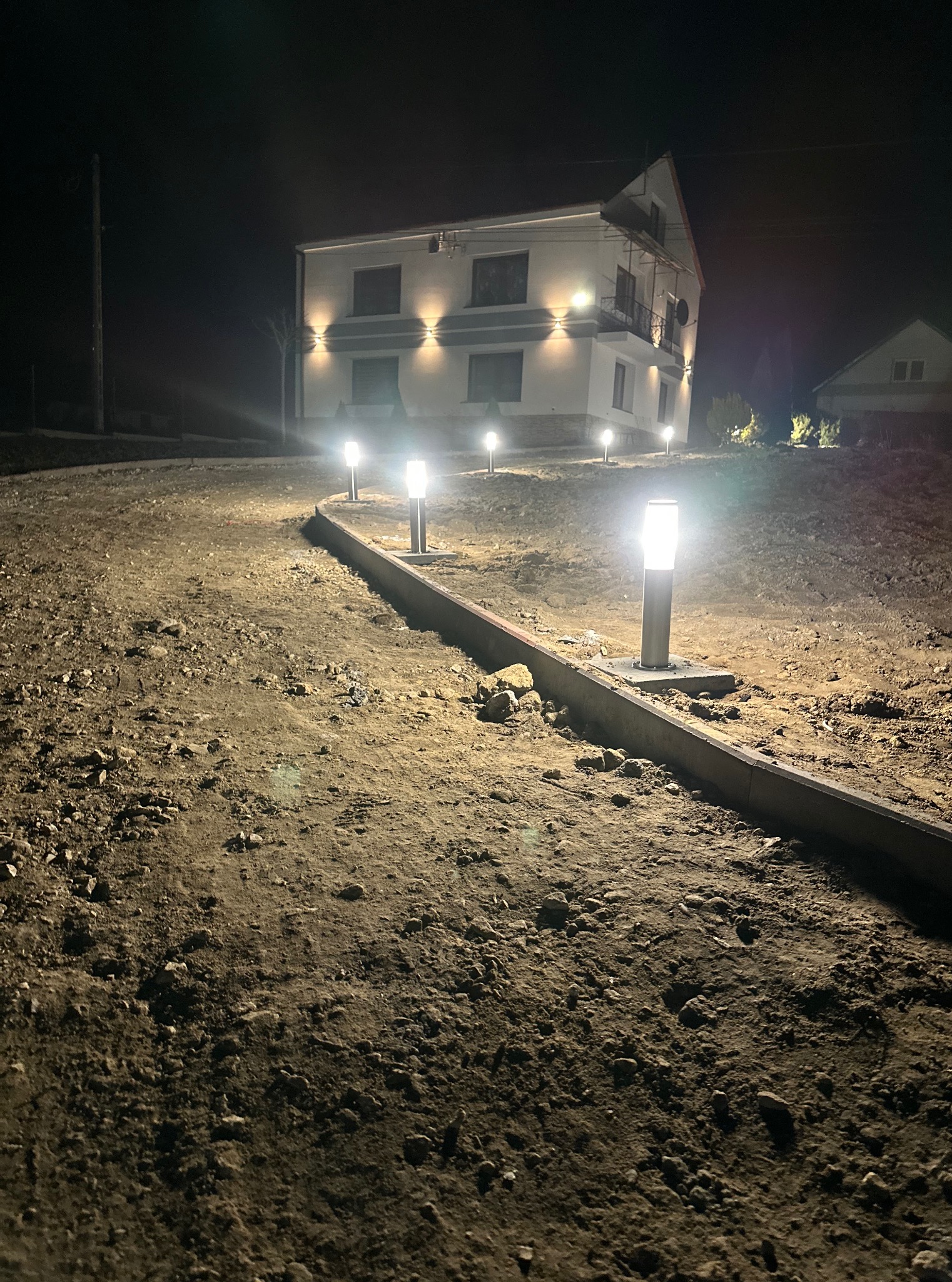 Nocny widok na posesję z oświetloną ścieżką i budynkiem z lampami zewnętrznymi. Oświetlenie posesji.