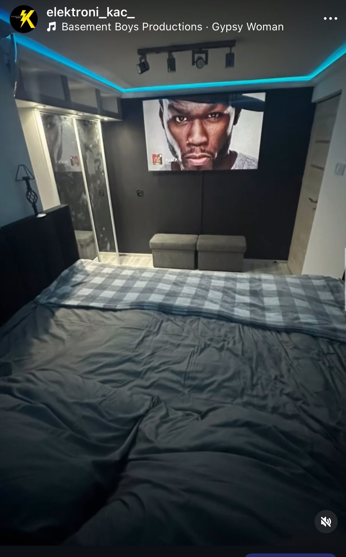 Nowoczesna sypialnia z podświetleniem LED sufitu, reflektorami i czarną ścianą z wizerunkiem 50 Centa. Minimalistyczny design, łóżko z szarą pościelą.