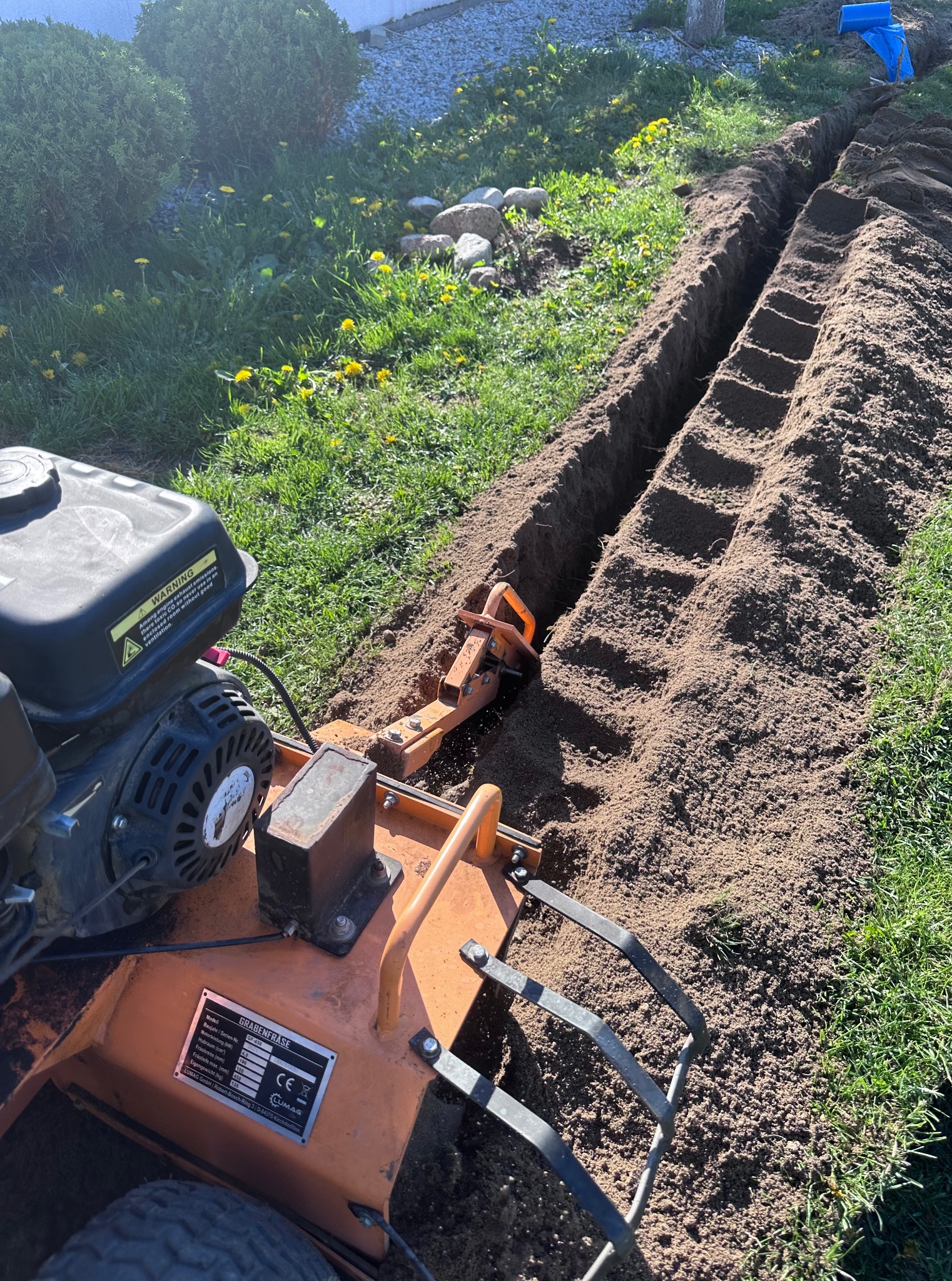 Frezarka do rowów marki Lumag GF-450 tworząca wąski wykop w trawniku, przygotowując teren pod instalacje. Widoczne świeżo wykopane rowy w ziemi.