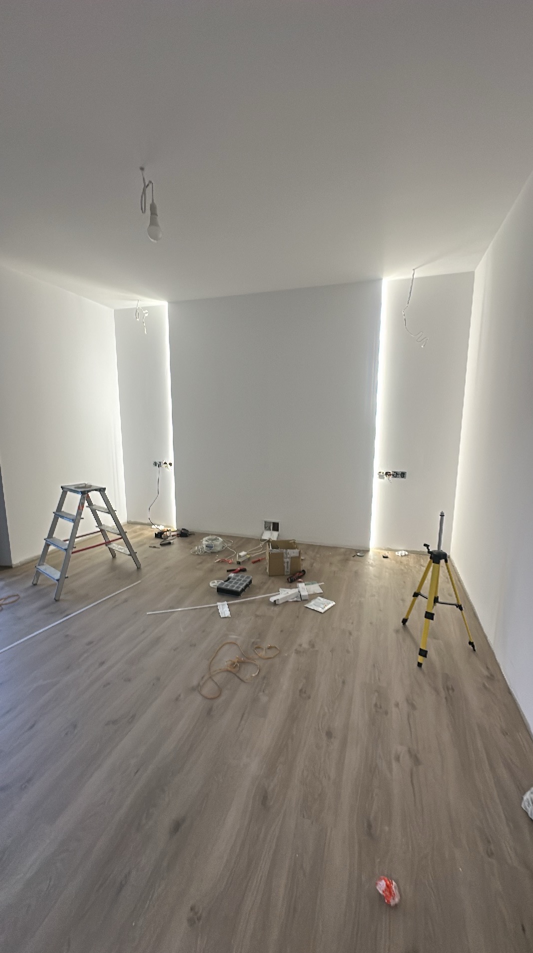 Prace elektryczne w nowym wnętrzu w Dąbrówce Wisłockiej: widoczne kable, puszki elektryczne, poziomica laserowa i drabina. Przygotowanie do montażu oświetlenia.