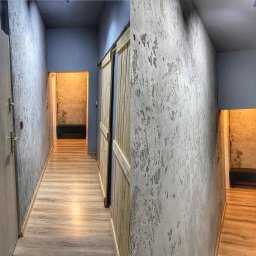 EMI Butik Kwiatowy Ewa Misiak - Korytarz po remoncie: drewniane drzwi przesuwne, podłoga drewnopodobna, ściany z efektem betonu architektonicznego i niebieski sufit. W tle widoczna ławka.