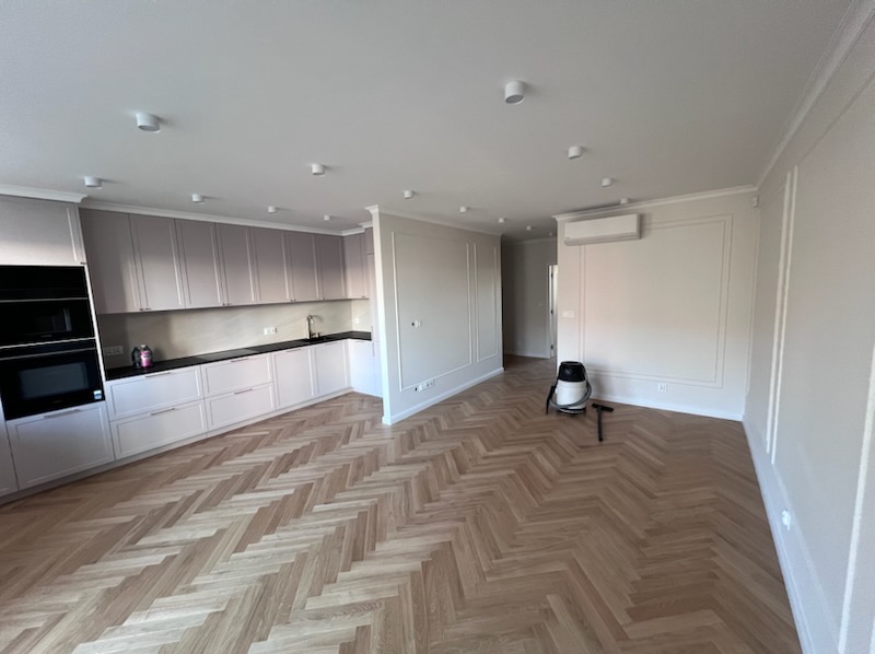 Jasne, przestronne wnętrze po remoncie w Krakowie: parkiet w jodełkę, zabudowa kuchenna w odcieniach szarości, subtelne sztukaterie i nowoczesne oświetlenie.