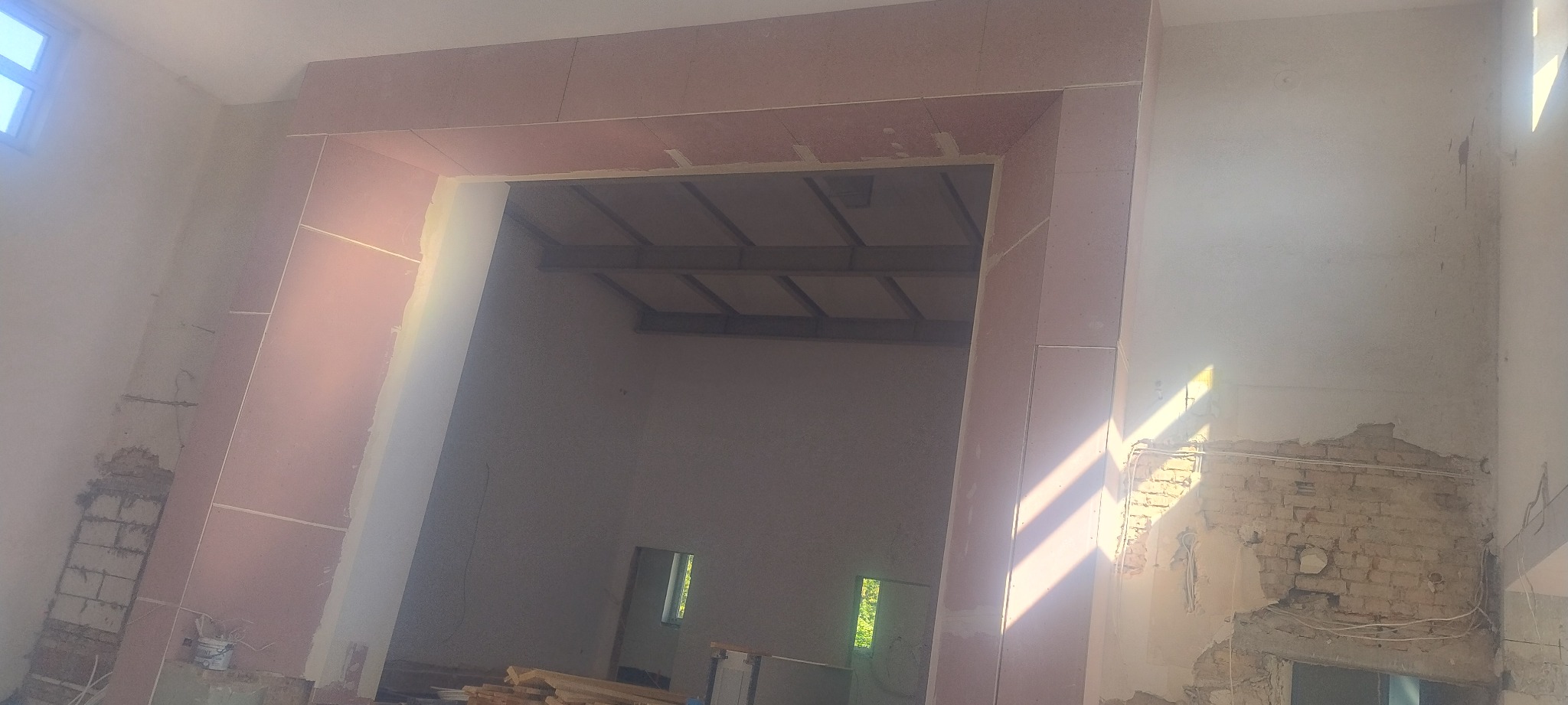 Wnętrze w trakcie remontu z zamontowanymi płytami kartonowo-gipsowymi tworzącymi obramowanie otworu drzwiowego. Widoczne surowe ściany i elementy konstrukcyjne.