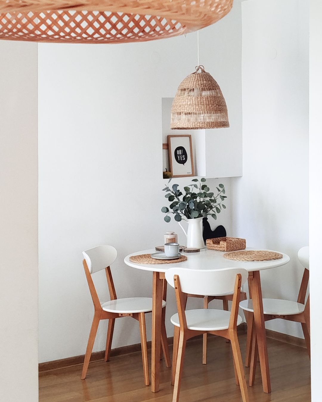 Jasna jadalnia: okrągły stół z drewnianymi krzesłami, plecione lampy i dekoracje w niszach. Minimalistyczny, skandynawski styl.