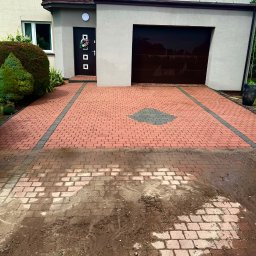PPHU Eco&Clean Grzegorz Blat - Częściowo umyta kostka brukowa na podjeździe przed domem jednorodzinnym. Widoczna różnica w czystości kostki, od brudnej po czystą, z wzorem z szarej kostki.