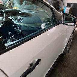 Eko myjka - Białe auto Renault Megane Cabriolet z czarną klamką i lusterkiem bocznym. Widoczne wnętrze pojazdu przez szybę. Opona na ścianie garażu w tle.