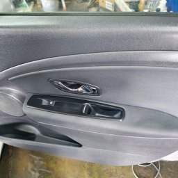 Eko myjka - Szczegółowe ujęcie wewnętrznej strony drzwi samochodu, z widoczną chromowaną klamką, panelem sterowania szybami i głośnikiem. Teksturowana powierzchnia tworzywa.