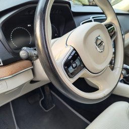 Eko myjka - Kremowa kierownica Volvo z czarnymi elementami sterującymi, widoczny kokpit i skórzana tapicerka. Detale wnętrza luksusowego auta.