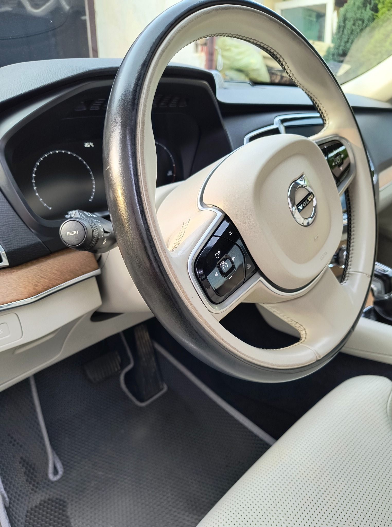 Kremowa kierownica Volvo z czarnymi elementami sterującymi, widoczny kokpit i skórzana tapicerka. Detale wnętrza luksusowego auta.