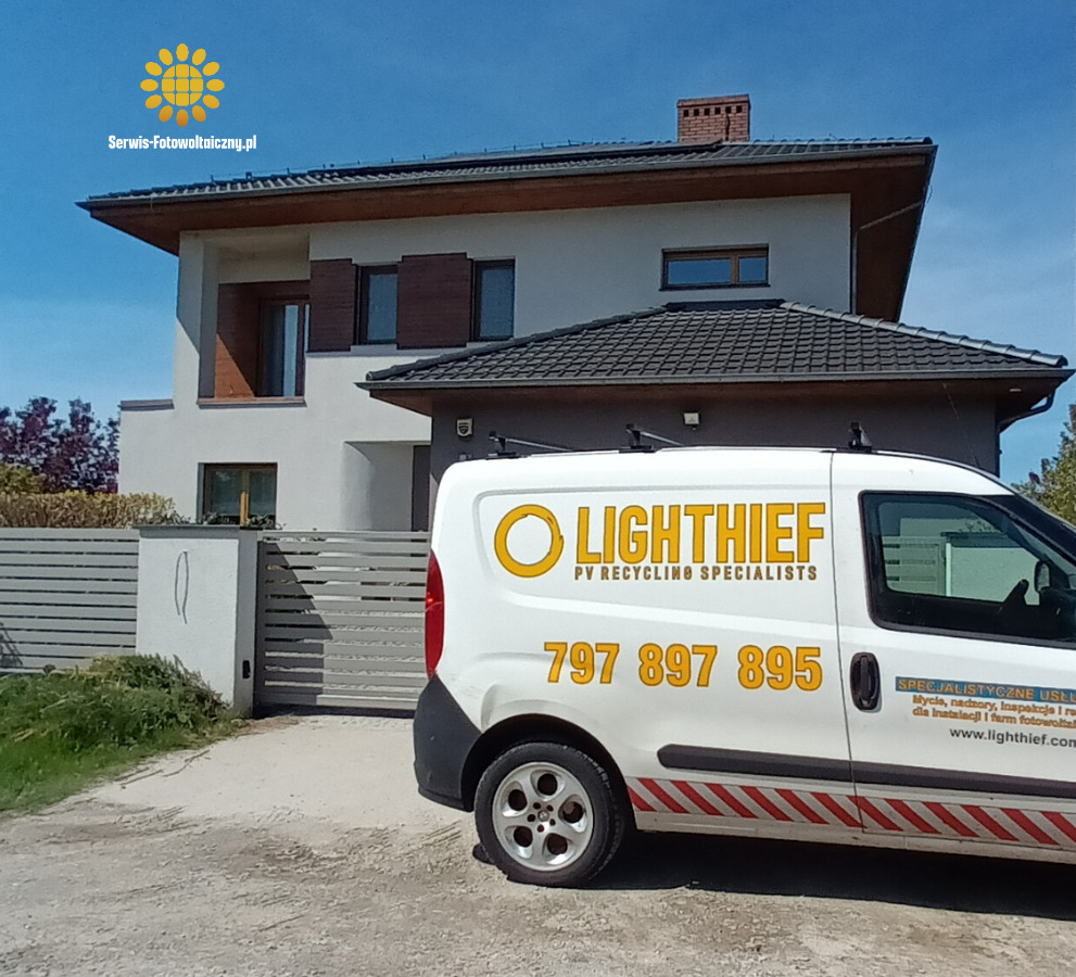 Biały bus firmy serwisującej fotowoltaikę przed domem jednorodzinnym. Na busie logo firmy i numer telefonu. Słoneczny dzień, błękitne niebo.