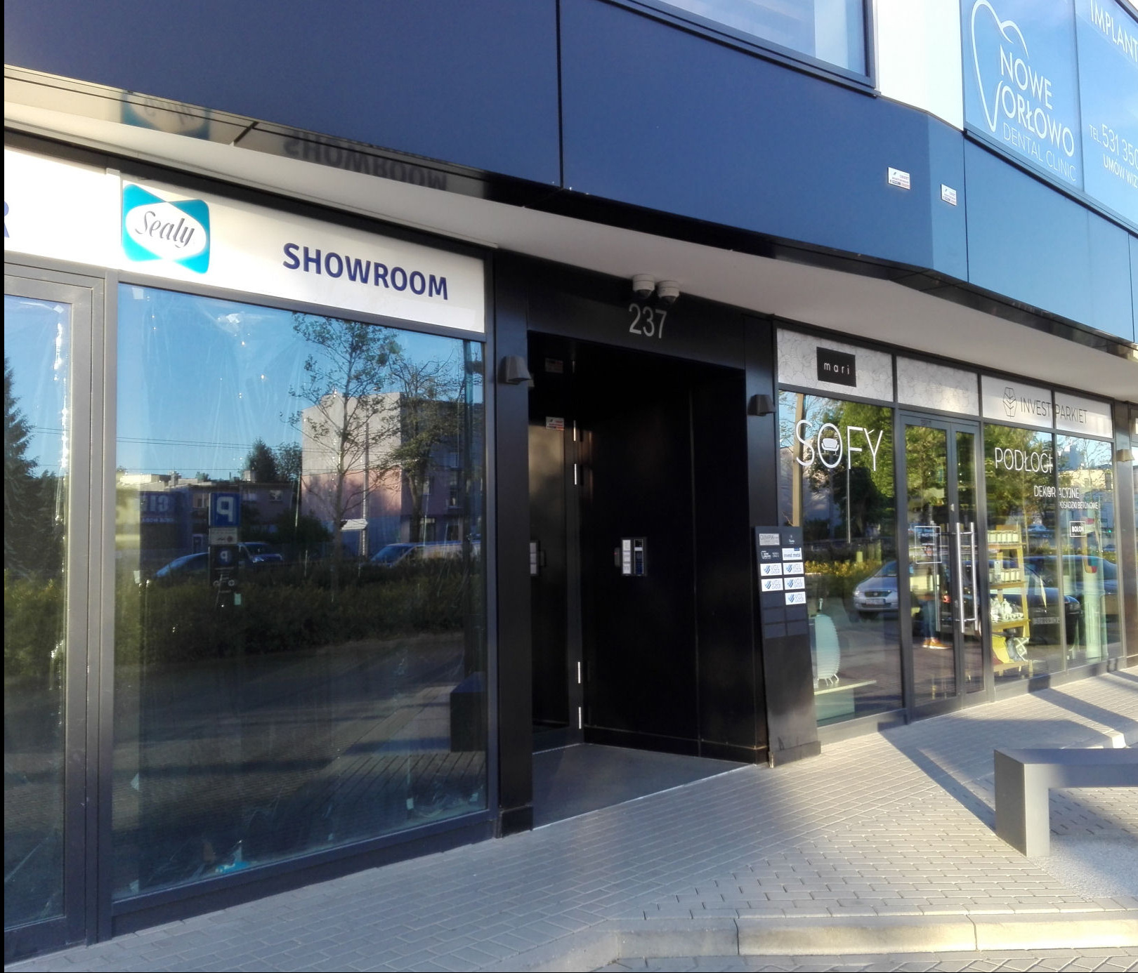 Fasada nowoczesnego budynku z numerem 237 i witrynami sklepów: Sealy Showroom, Nowe Orłowo Dental Clinic, Sofy Invest Parkiet Podłogi.