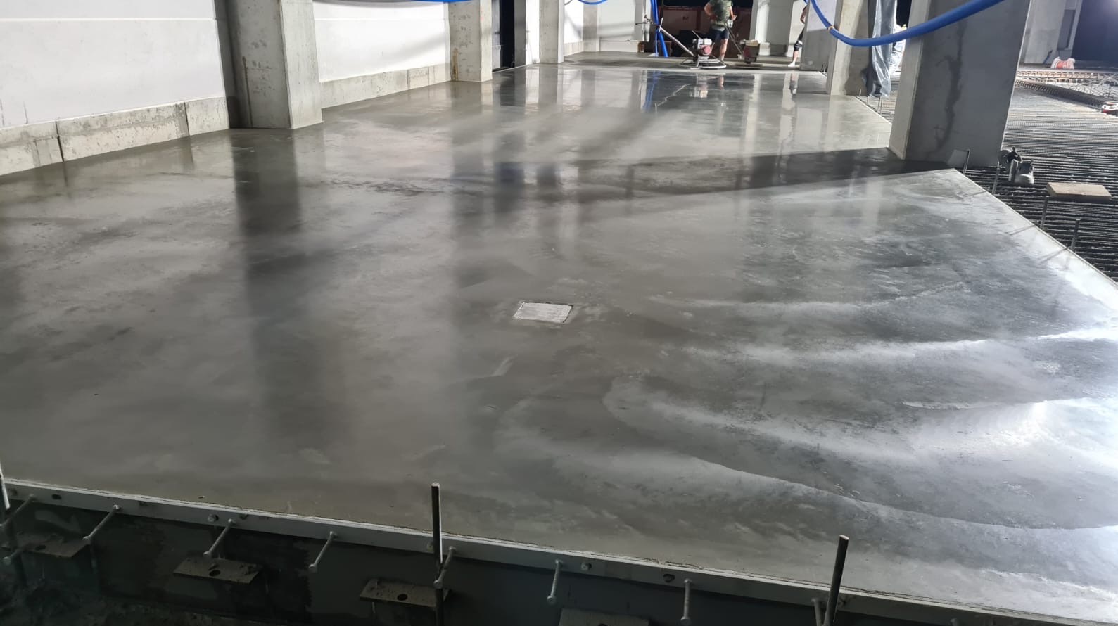 Gładka, szara powierzchnia wylewki w Kaniowie, z widocznymi refleksami światła i elementami konstrukcyjnymi w tle, ukazująca etap prac wykończeniowych.