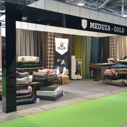 Meduza Mateusz Wycech - Ekspozycja stoiska Meduza-Gold na targach: różnorodne legowiska dla zwierząt, zasłony w tle, osoby w garniturach, zielona podłoga. Prezentacja produktów.