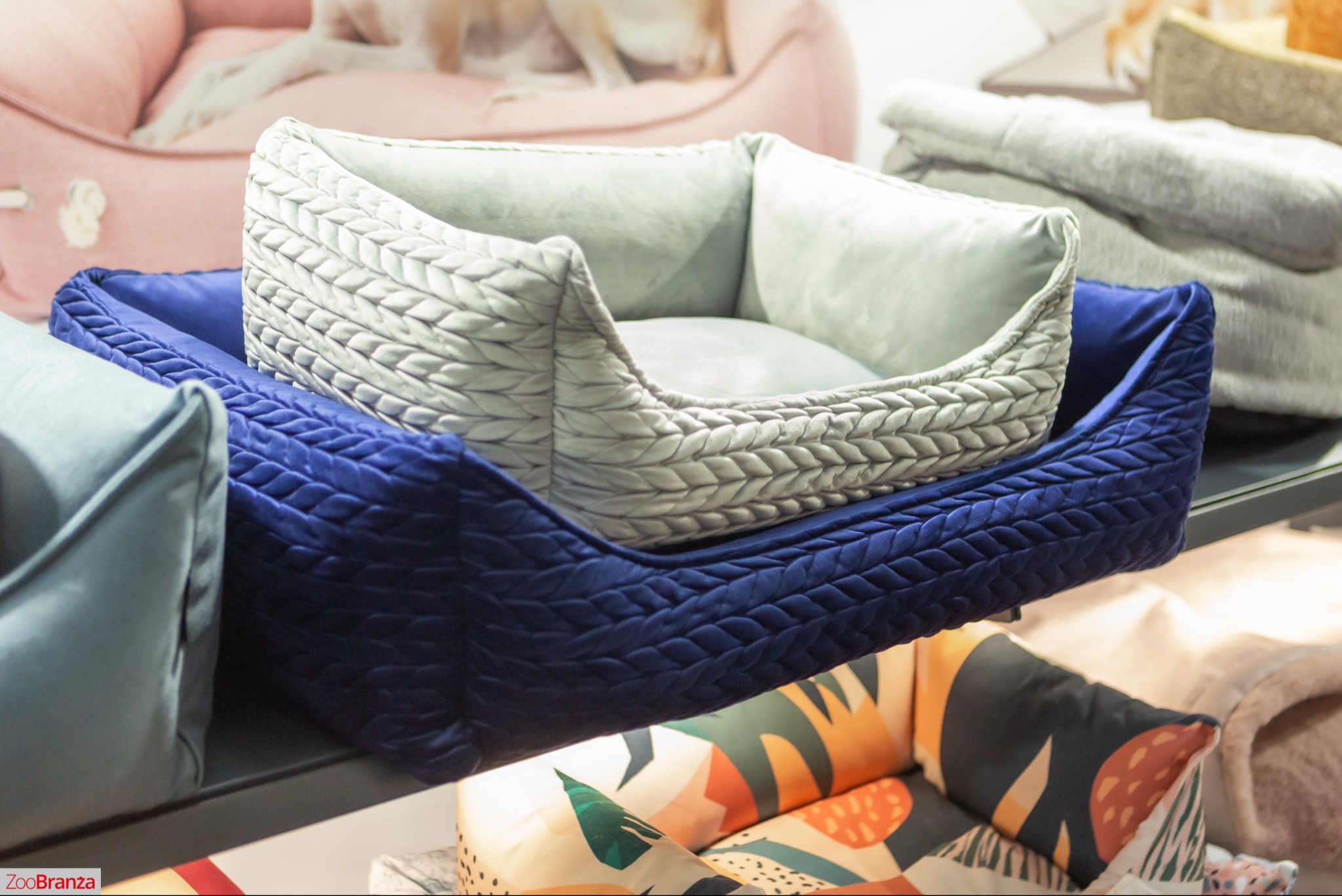 Kaskadowe ułożenie pluszowych legowisk dla zwierząt w odcieniach szarości i granatu, z dekoracyjnym pikowaniem, na tle innych akcesoriów dla zwierząt.