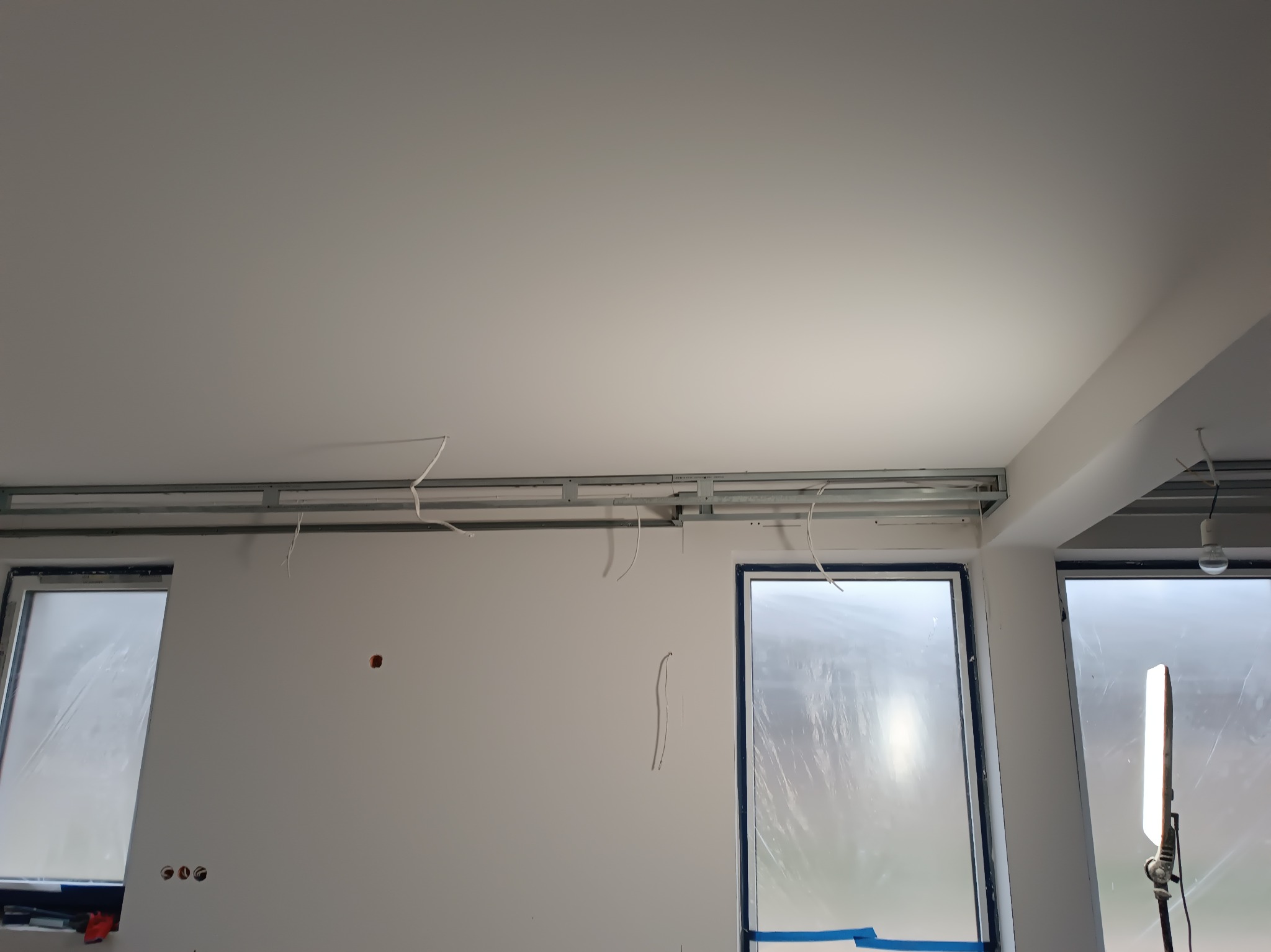 Montaż profili sufitowych podwieszanych z widocznymi przewodami elektrycznymi, okna zabezpieczone folią malarską, ściany przygotowane do malowania.