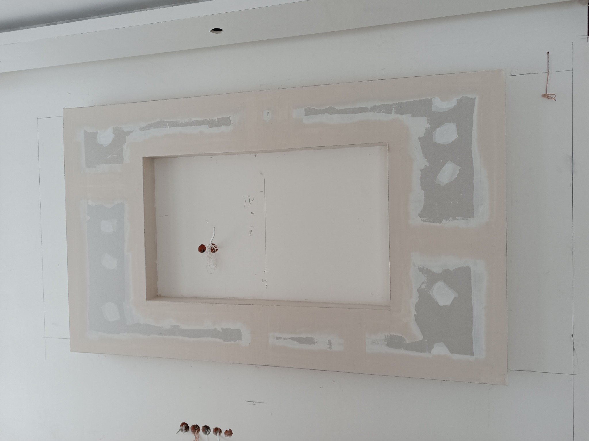 Ściana z płyt karton-gips z wyciętym prostokątnym otworem na telewizor, widoczne ślady szpachlowania i instalacja elektryczna. Etap prac wykończeniowych.