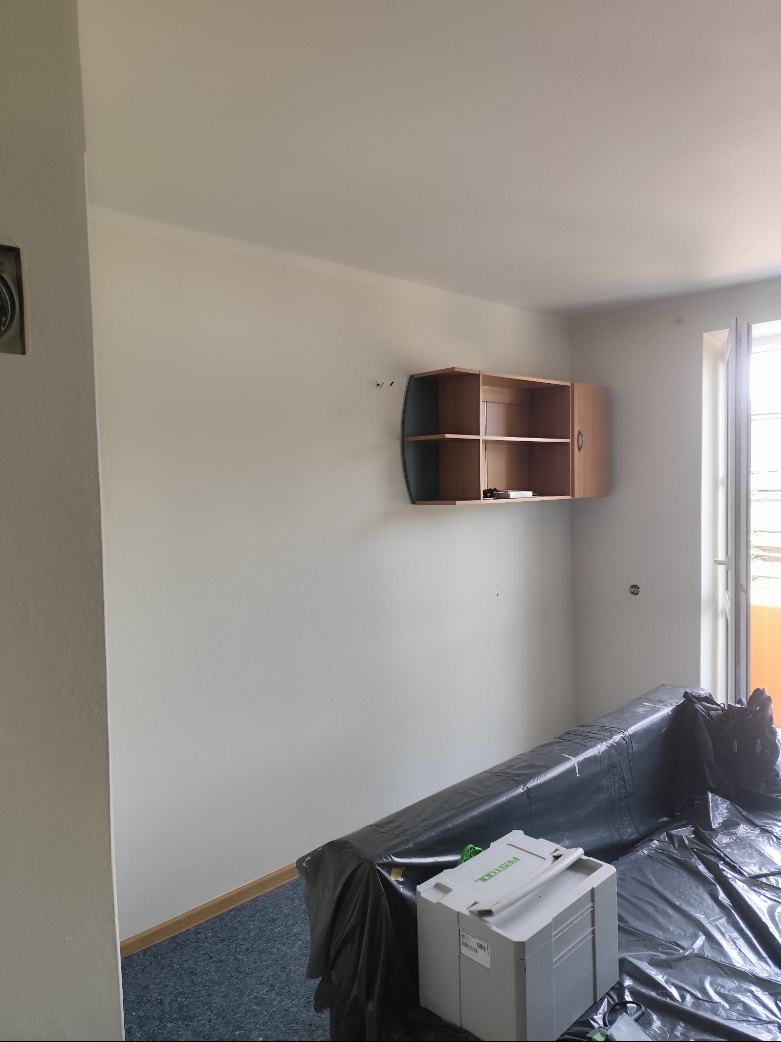 Pokój w trakcie przygotowań do malowania: ściany zabezpieczone folią, widoczna szafka na ścianie i skrzynka narzędziowa Festool. Przygotowanie do remontu.