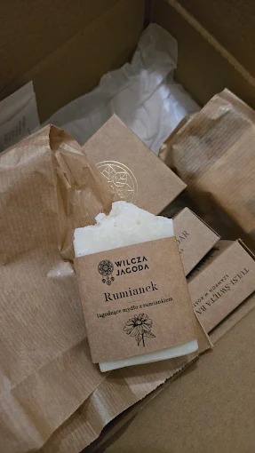 Ręcznie robione mydło rumiankowe Wilcza Jagoda w brązowym opakowaniu, w kartonowym pudełku z innymi produktami. Naturalne kosmetyki.