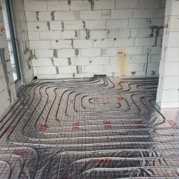 HYDRAULIK Meik Barwinski - Ułożone rury ogrzewania podłogowego na folii z siatką, widok z góry, ściany z betonu komórkowego w surowym stanie, instalacja w budynku w trakcie budowy.