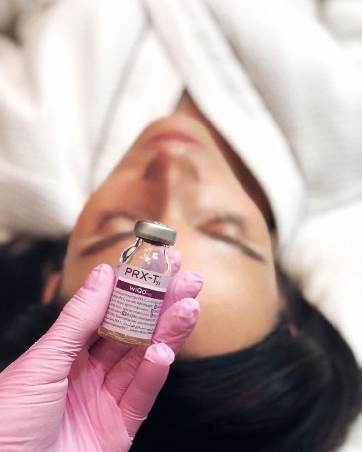 Klientka przed zabiegiem PRX-T33, w rękawiczce trzymana fiolka preparatu. Widoczny dekolt w ręczniku. Delikatne, naturalne światło.