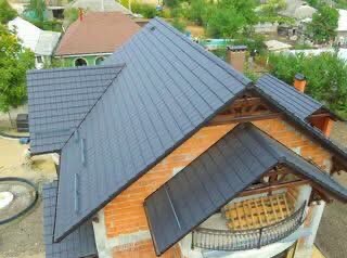 Nowy, ciemnoszary dach z blachodachówki na budynku z surowej cegły, widok z góry. W tle zabudowa jednorodzinna i zieleń drzew.