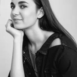 Czarno-biały portret kobiety z długimi włosami, opierającej brodę na dłoni w Słupsku. Ubrana w jeansową kurtkę z wycięciem na ramieniu, patrzy w obiektyw.