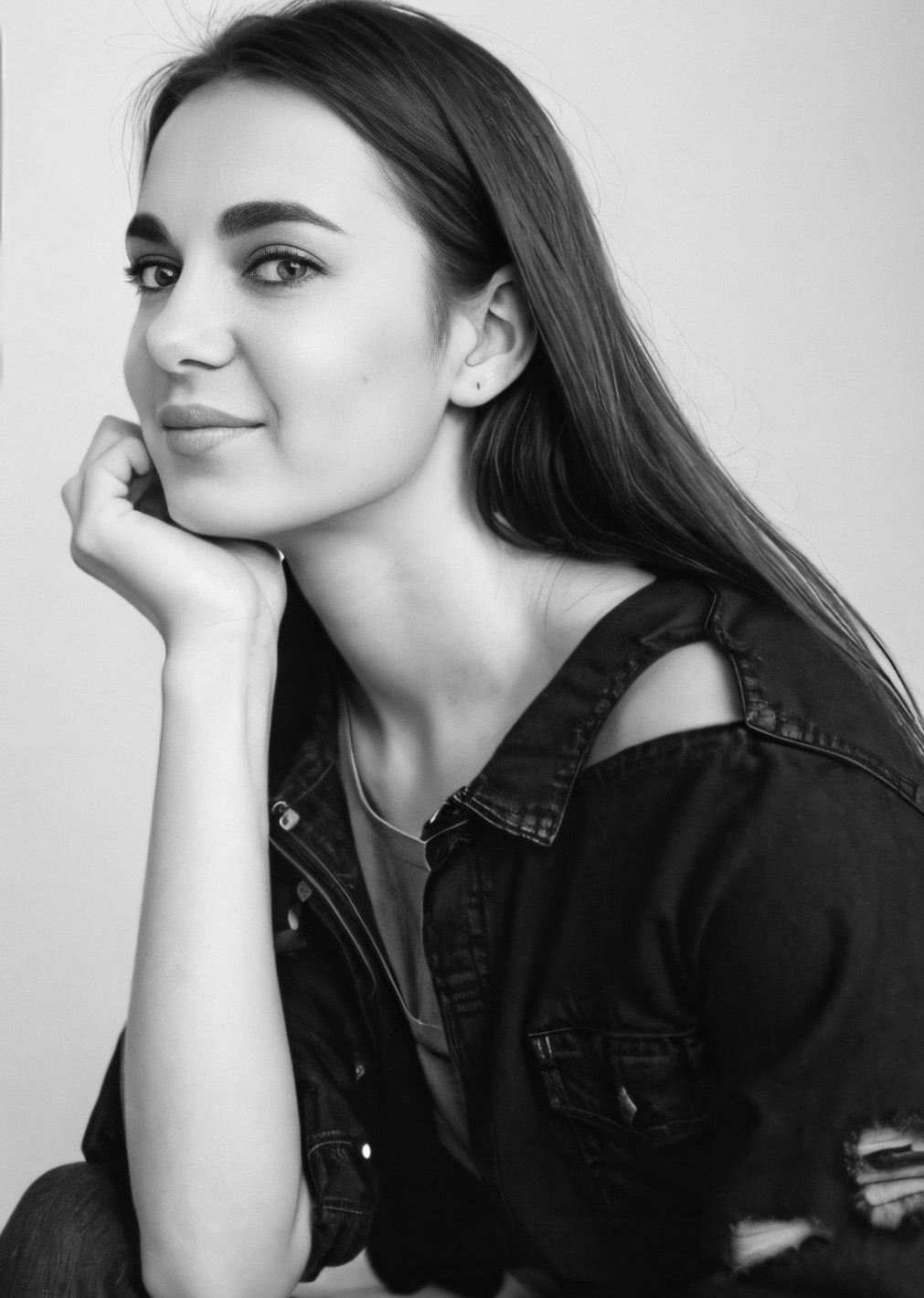 Czarno-biały portret kobiety z długimi włosami, opierającej brodę na dłoni w Słupsku. Ubrana w jeansową kurtkę z wycięciem na ramieniu, patrzy w obiektyw.