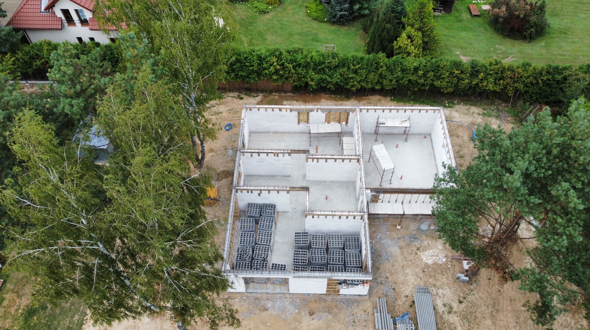 Fundamenty domu jednorodzinnego z betonu komórkowego, widziane z góry w Niemcach. Częściowo wzniesione ściany, rusztowania i bloczki. Etap budowy.