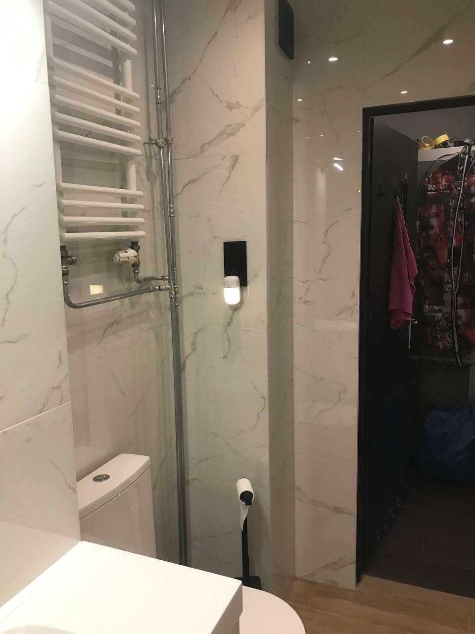 Nowoczesna łazienka z marmurowymi płytkami, grzejnikiem drabinkowym i toaletą. Widoczny fragment wnętrza z akcesoriami.