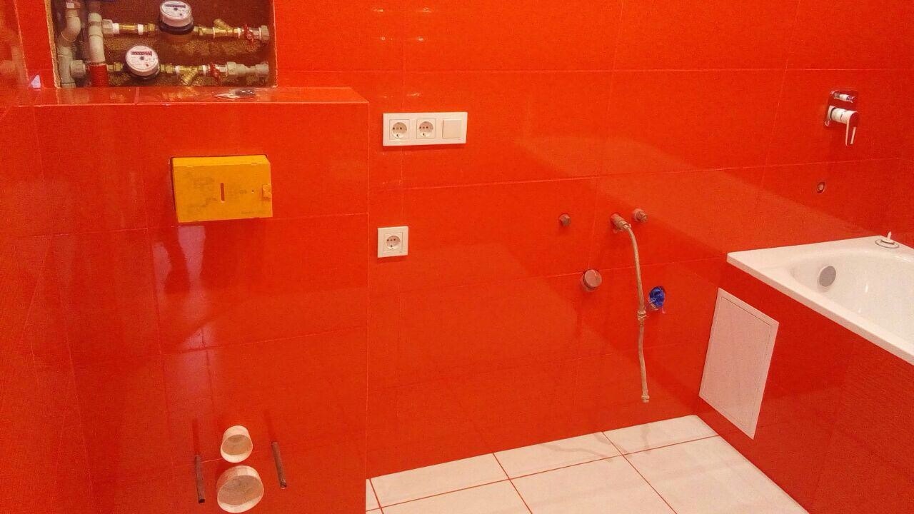 Pomarańczowa łazienka po remoncie: płytki ceramiczne, biała wanna, punkty elektryczne i instalacja wodno-kanalizacyjna. Nowoczesne wykończenie wnętrza.