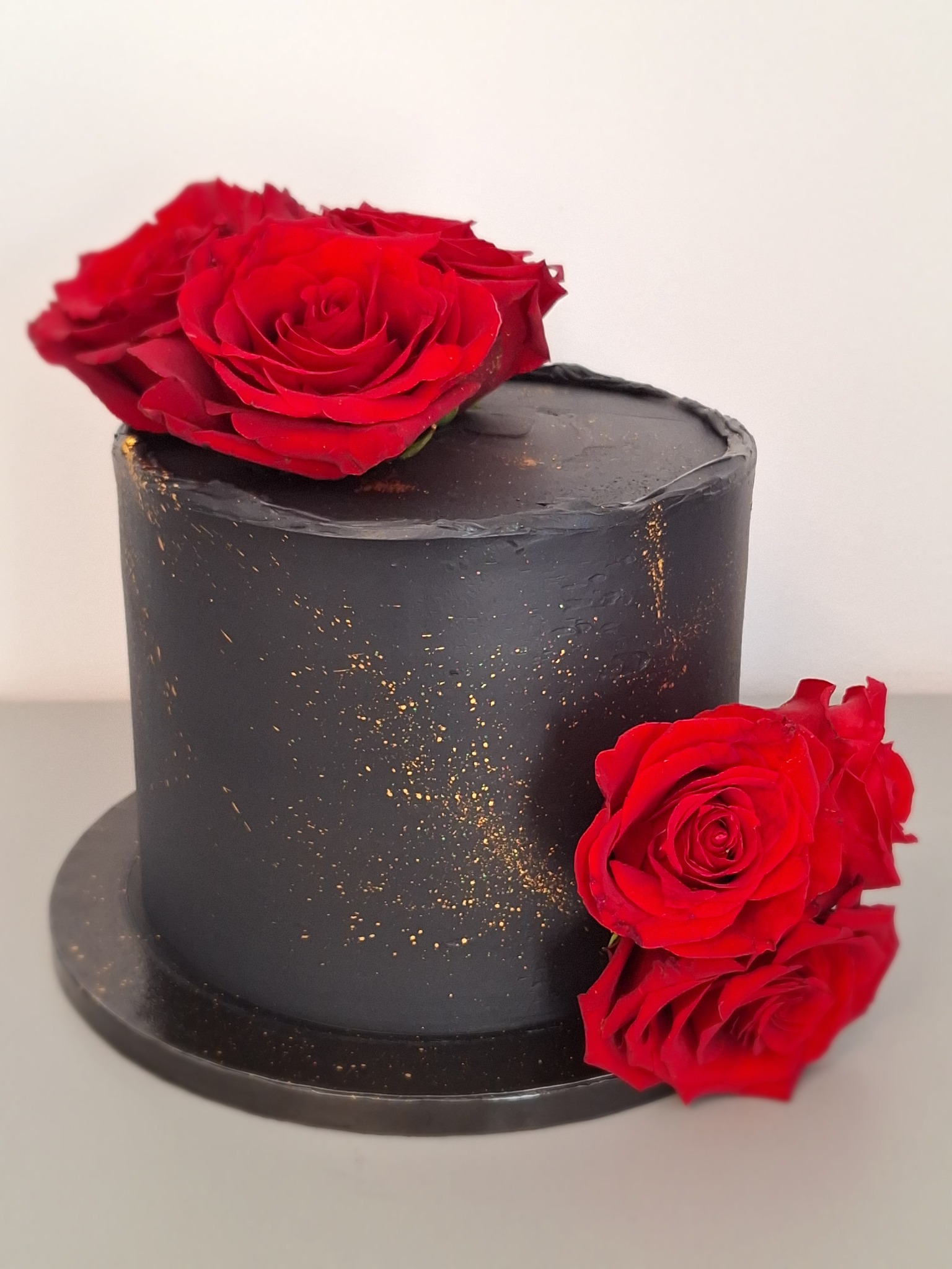 Czarny tort z efektem ombre, zdobiony złotymi drobinkami i czerwonymi różami. Elegancki wypiek na uroczystość, z bliska.