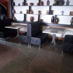 WOODSOFT - Czarne, tapicerowane loże z białymi stolikami w lokalu. W tle półki z dekoracyjnymi naczyniami. Widok na podłogę z szarego lastryko i dystrybutor napojów.