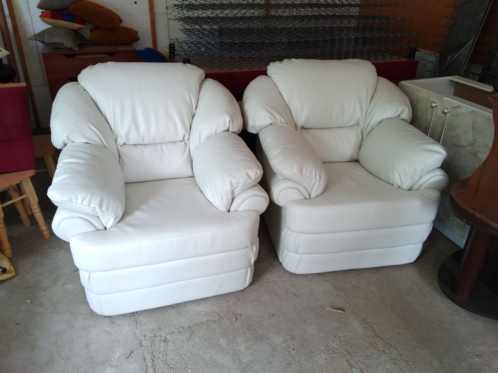 Dwa białe, skórzane fotele klubowe z charakterystycznymi, zaokrąglonymi podłokietnikami, ustawione obok siebie na szarym tle. Widoczne elementy wyposażenia wnętrza.