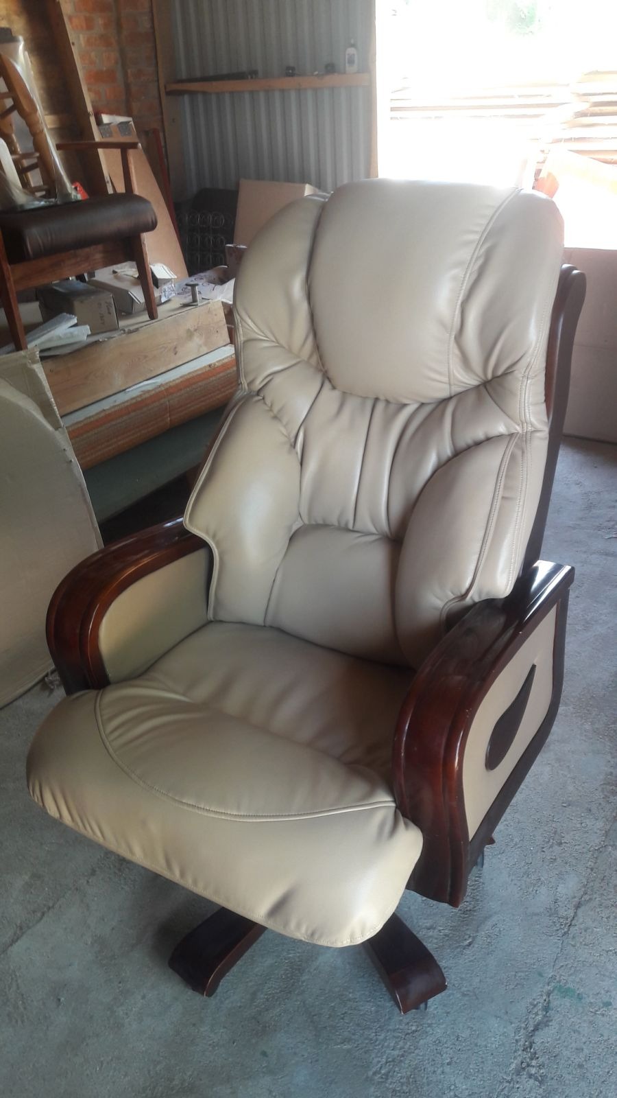 Beżowy, skórzany fotel obrotowy z drewnianymi elementami, widoczny z bliska na tle pomieszczenia gospodarczego, prezentujący detale wykończenia.