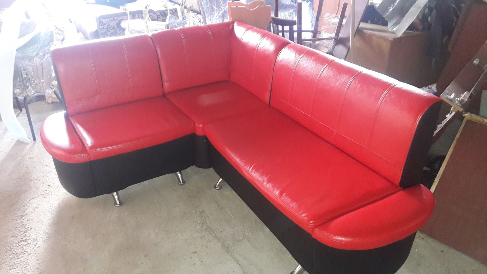 Czerwono-czarny narożnik z ekoskóry na metalowych nóżkach, widoczny w warsztacie tapicerskim. Odnowiony mebel po renowacji tapicerskiej.