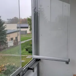 Otwarta, przesuwna zabudowa balkonu z profili aluminiowych i szkła. Widok na zewnątrz przez częściowo otwarte panele.