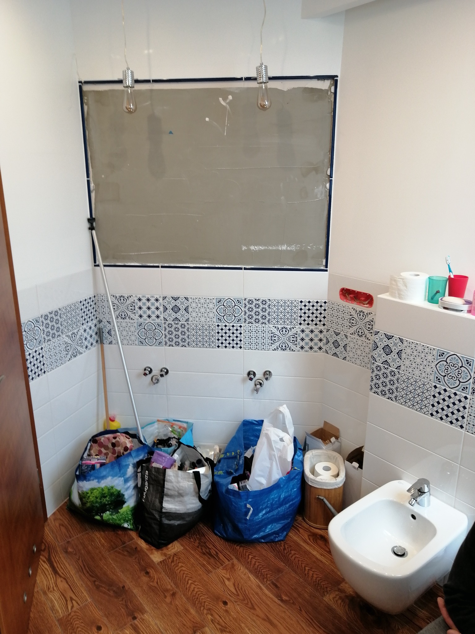 Łazienka w trakcie prac: ściany z częściowo położonymi płytkami, przygotowane miejsce pod lustro, worki z odpadami, bidet. Widoczne niedokończone etapy prac.
