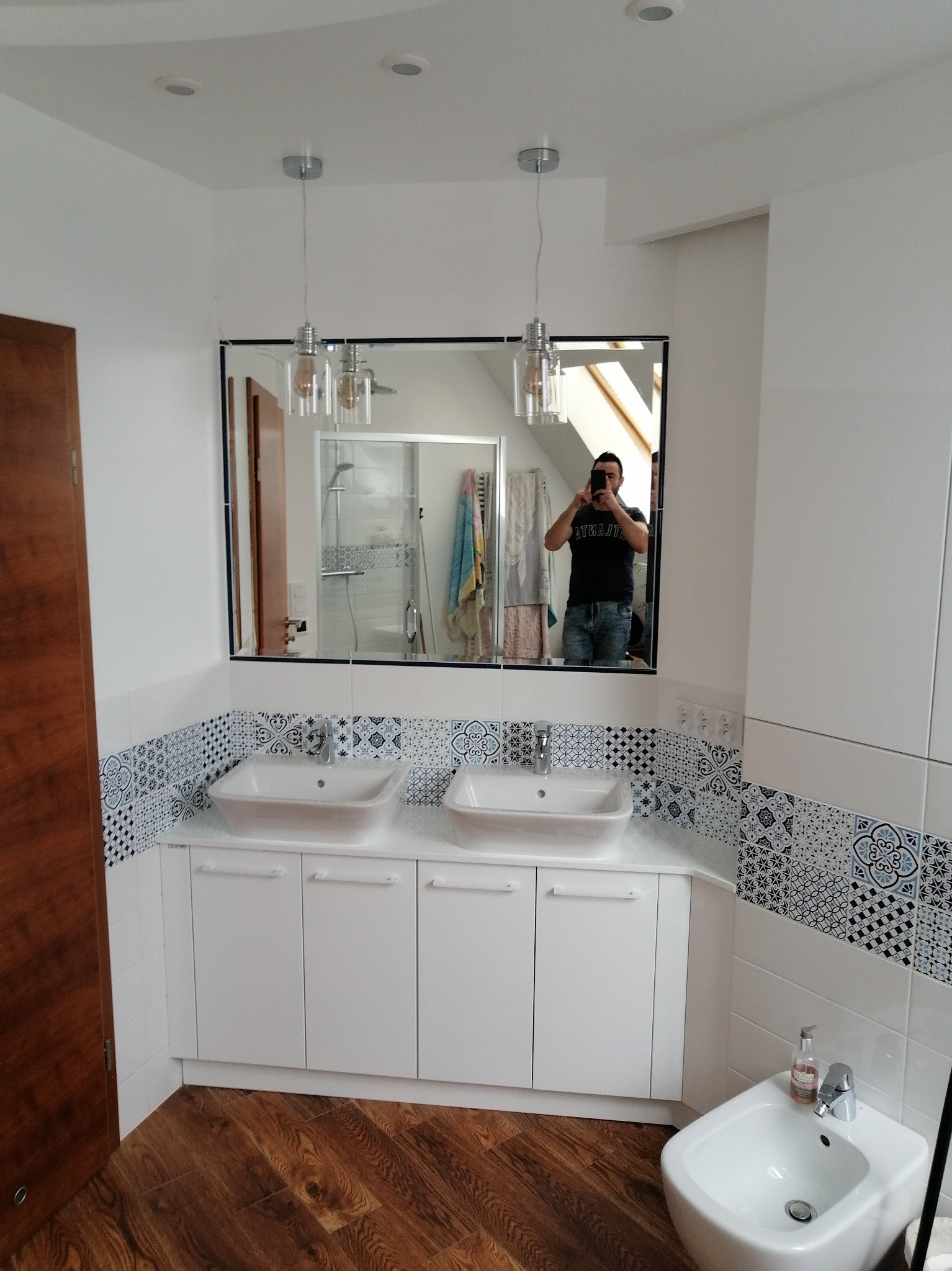 Wykończona łazienka z dwiema umywalkami nablatowymi, szafką pod umywalkami, bidetem i lustrem z odbijającą się osobą robiącą zdjęcie telefonem.