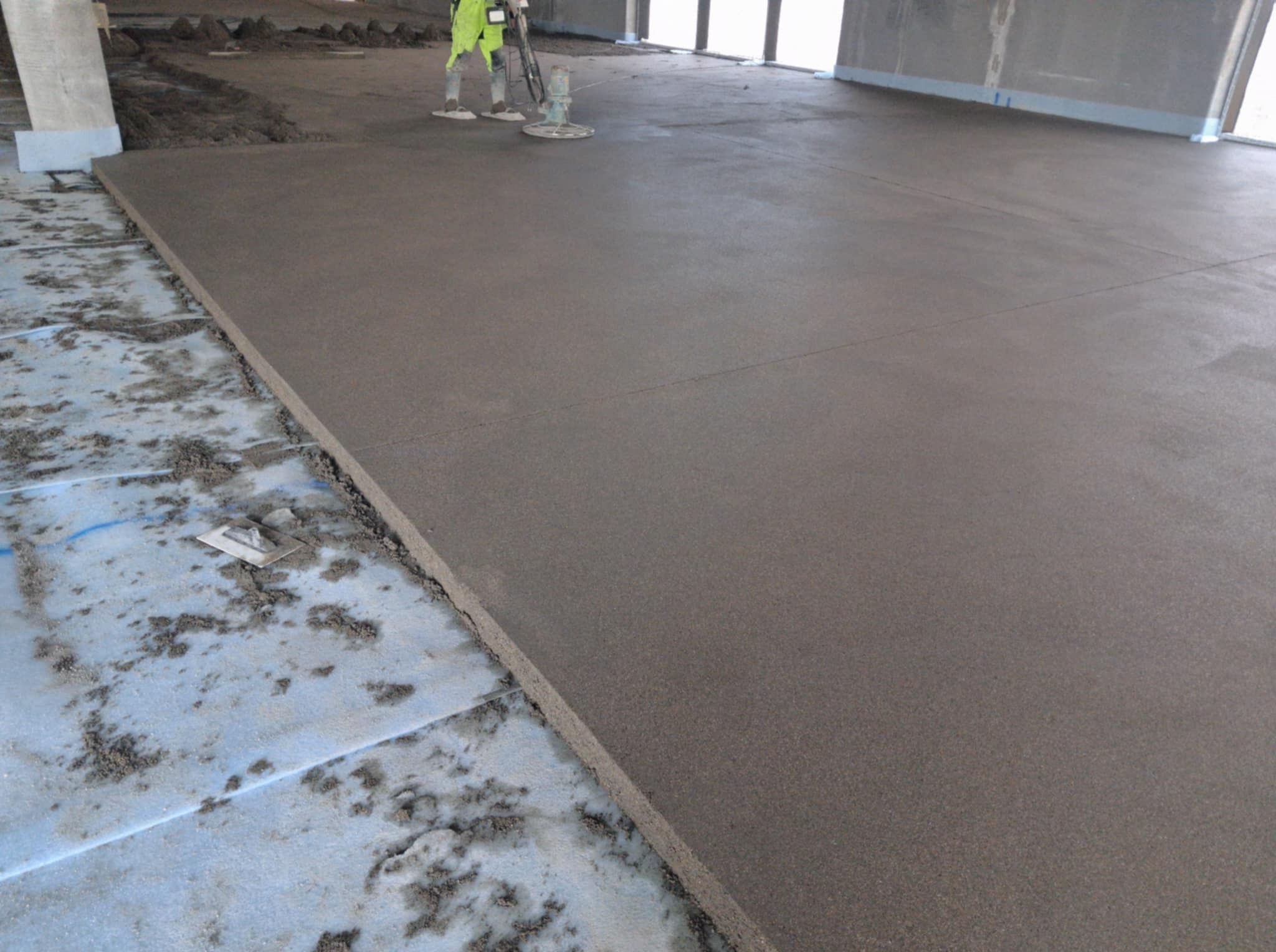 Wyrównywanie świeżo wylanej posadzki jastrychowej za pomocą zacieraczki mechanicznej. Widoczne nierówności podłoża i narzędzia. Praca w trakcie realizacji.