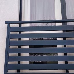 KriStalSpaw - Nowoczesna, grafitowa balustrada balkonowa z poziomych profili, zamontowana na tle białej elewacji i okna z firanką. Minimalistyczny design.