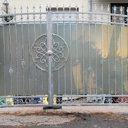 KriStalSpaw - Elegancka, dwuskrzydłowa brama wjazdowa z dekoracyjnymi elementami i wypełnieniem z mlecznego szkła, osadzona na ceglanych słupkach.