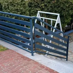 Nowoczesna, pozioma balustrada metalowa w kolorze grafitowym, zabezpieczająca schody zewnętrzne prowadzące do ogrodu. W tle widoczny huśtawka.