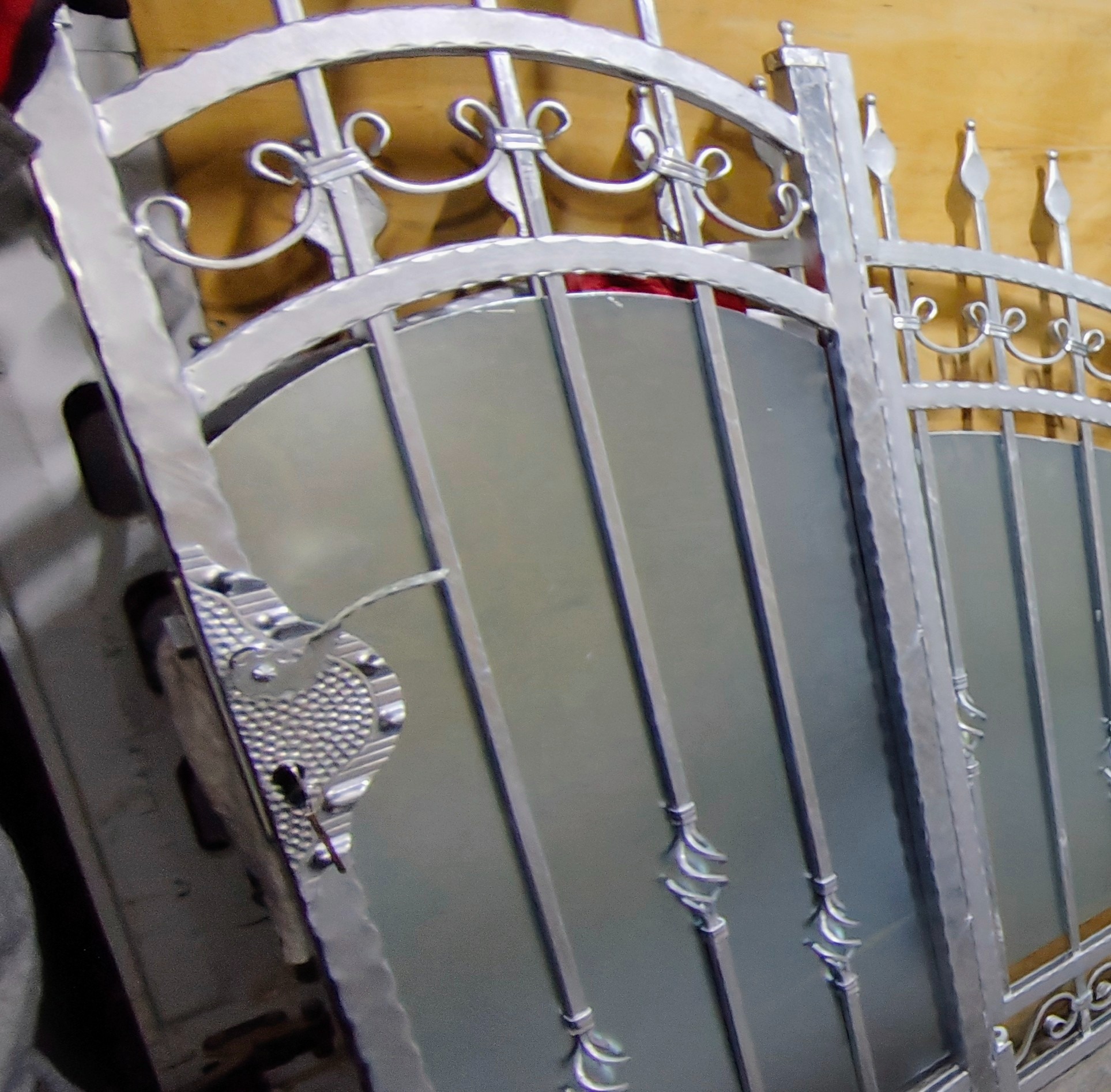 Dwie metalowe bramy z dekoracyjnymi elementami i zamkiem, ustawione obok siebie, w srebrnym odcieniu, gotowe do montażu. Widoczne detale wykończenia.