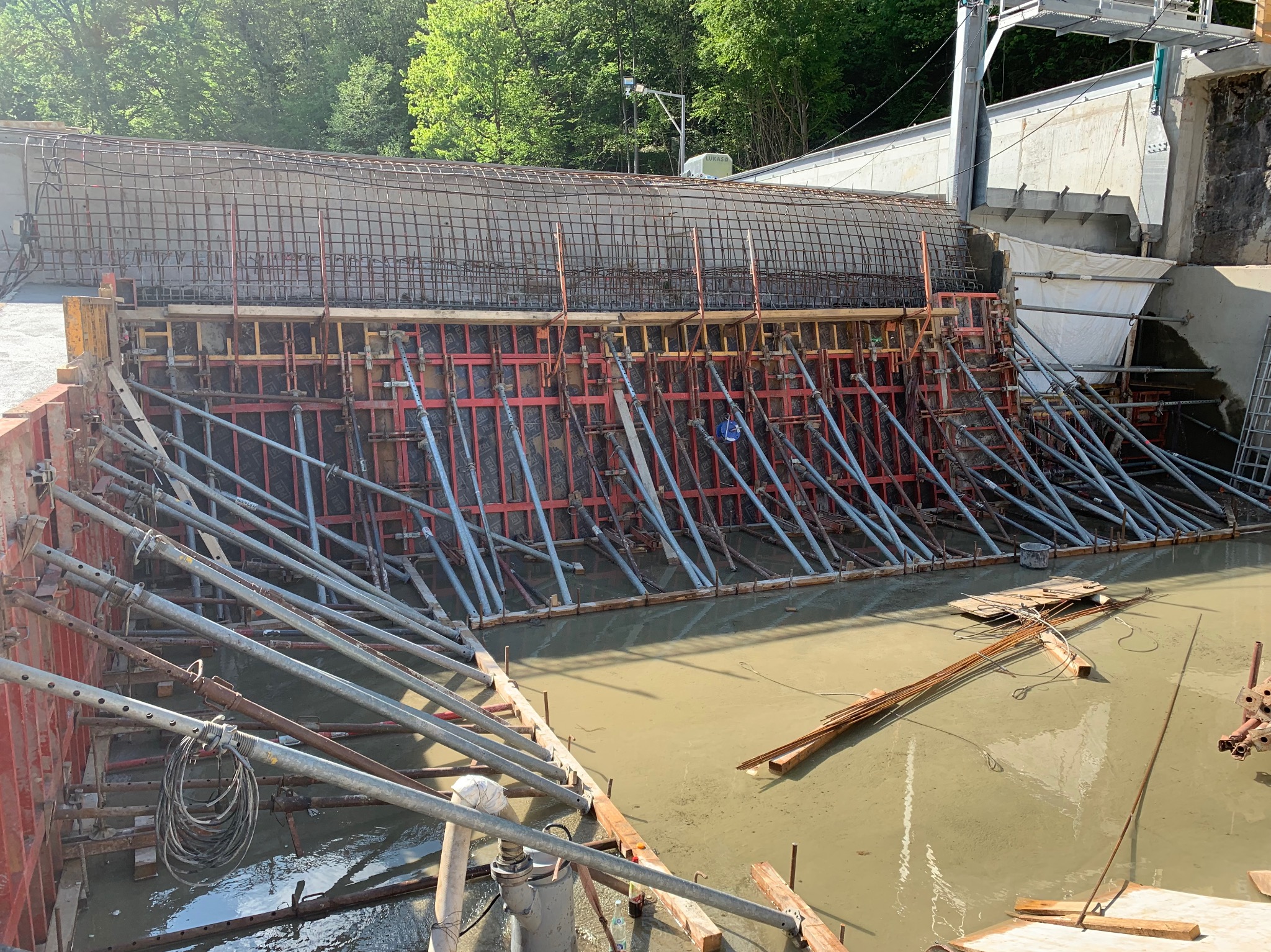 Budowa żelbetowej konstrukcji z widocznym zbrojeniem i szalunkiem, wsparta metalowymi stemplami w wodzie. Elementy konstrukcyjne w tle.